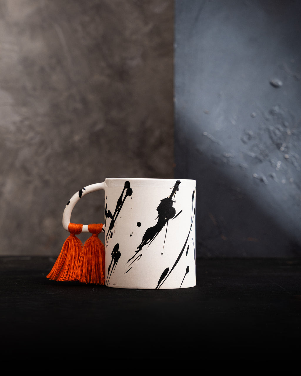 White mug with black abstract designs and an orange tassel
