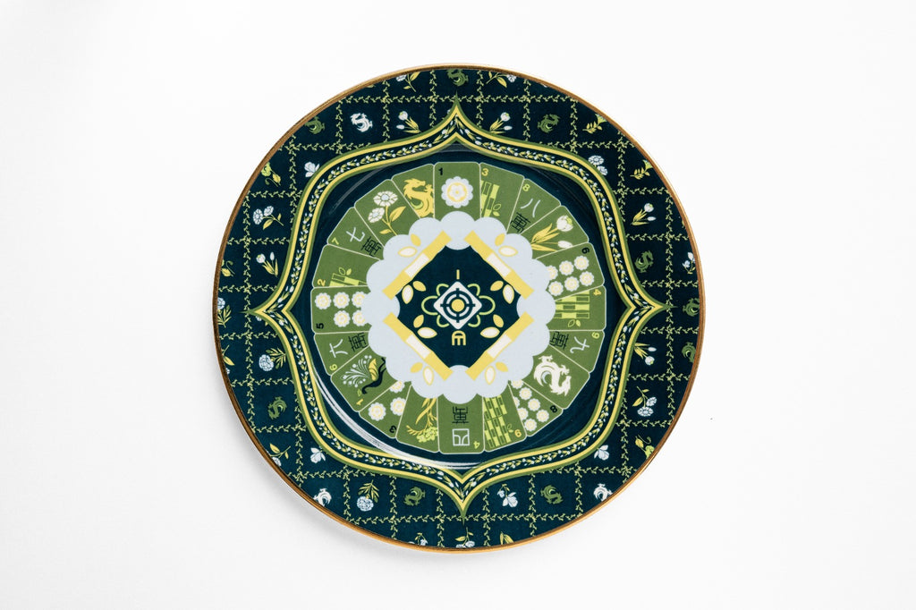 Overhead view of navy ceramic plate with gold decorative border, featuring layered geometric and botanical design with white and green floral center medallion
