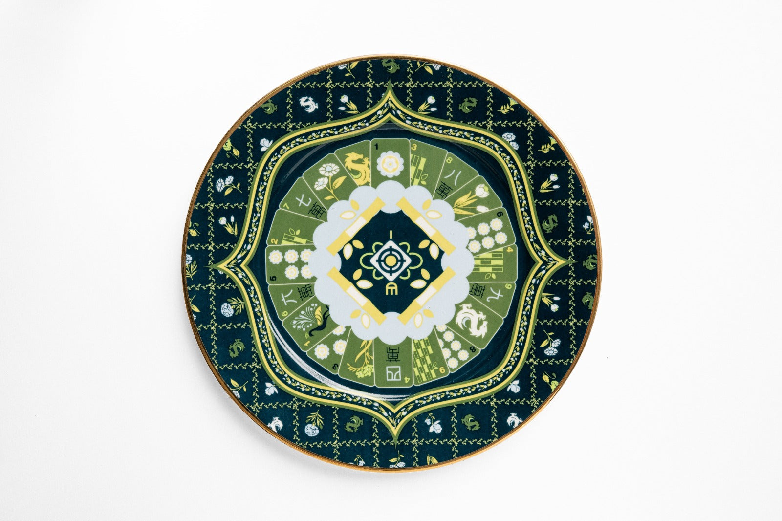 Overhead view of navy ceramic plate with gold decorative border, featuring layered geometric and botanical design with white and green floral center medallion