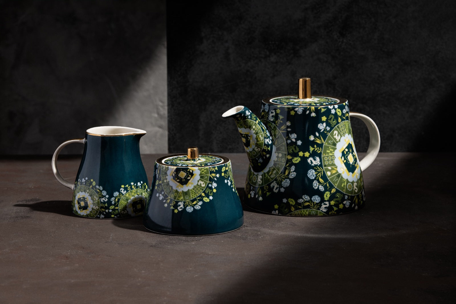 Navy blue porcelain teaware trio featuring green floral medallions, comprising a spouted teapot, milk jug, and covered sugar pot with gold finial