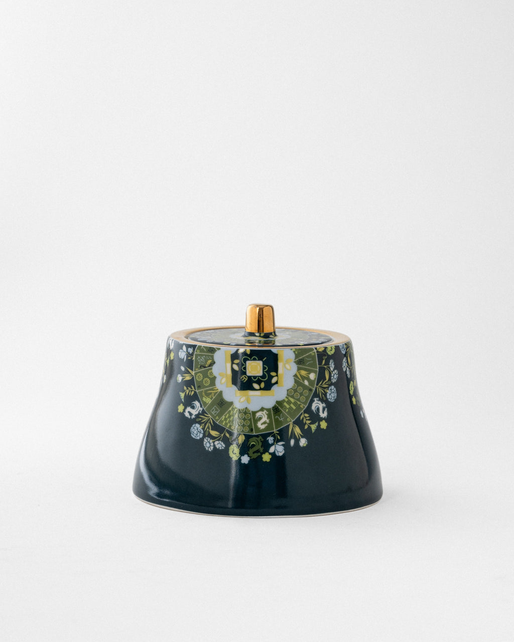 Navy ceramic covered sugar vessel with brass finial, featuring green and white botanical border band beneath gold-trimmed lid on neutral background