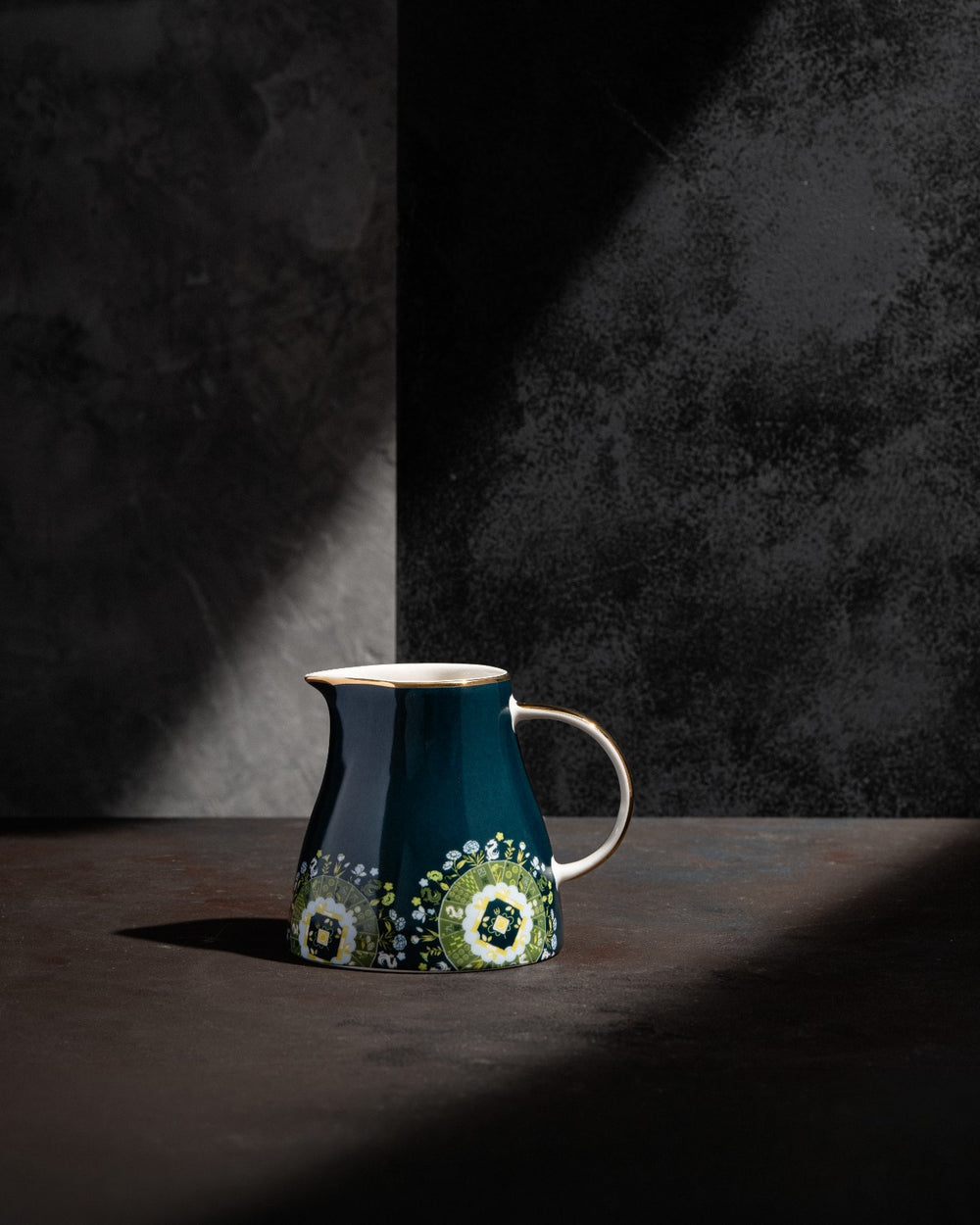 Navy ceramic teapot with beige handle and green floral design, studio lighting side view