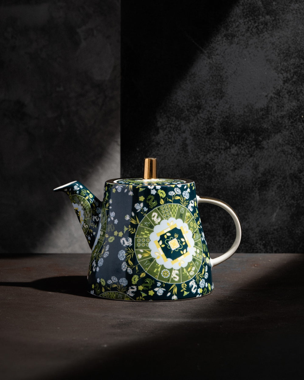 Navy teapot with wooden finial and handle, green floral motif, side view with studio lighting