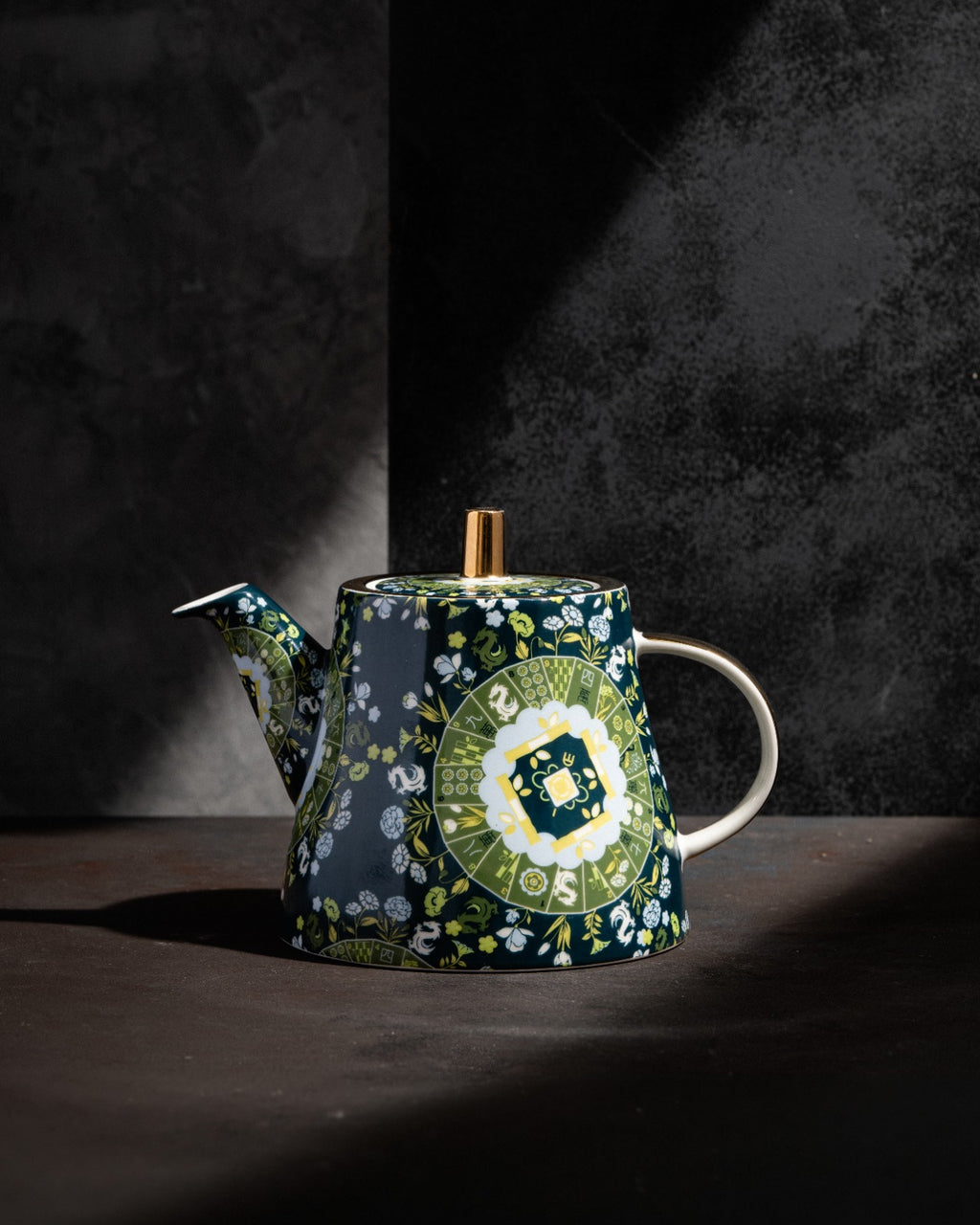 Navy teapot with wooden finial and handle, green floral motif, side view with studio lighting