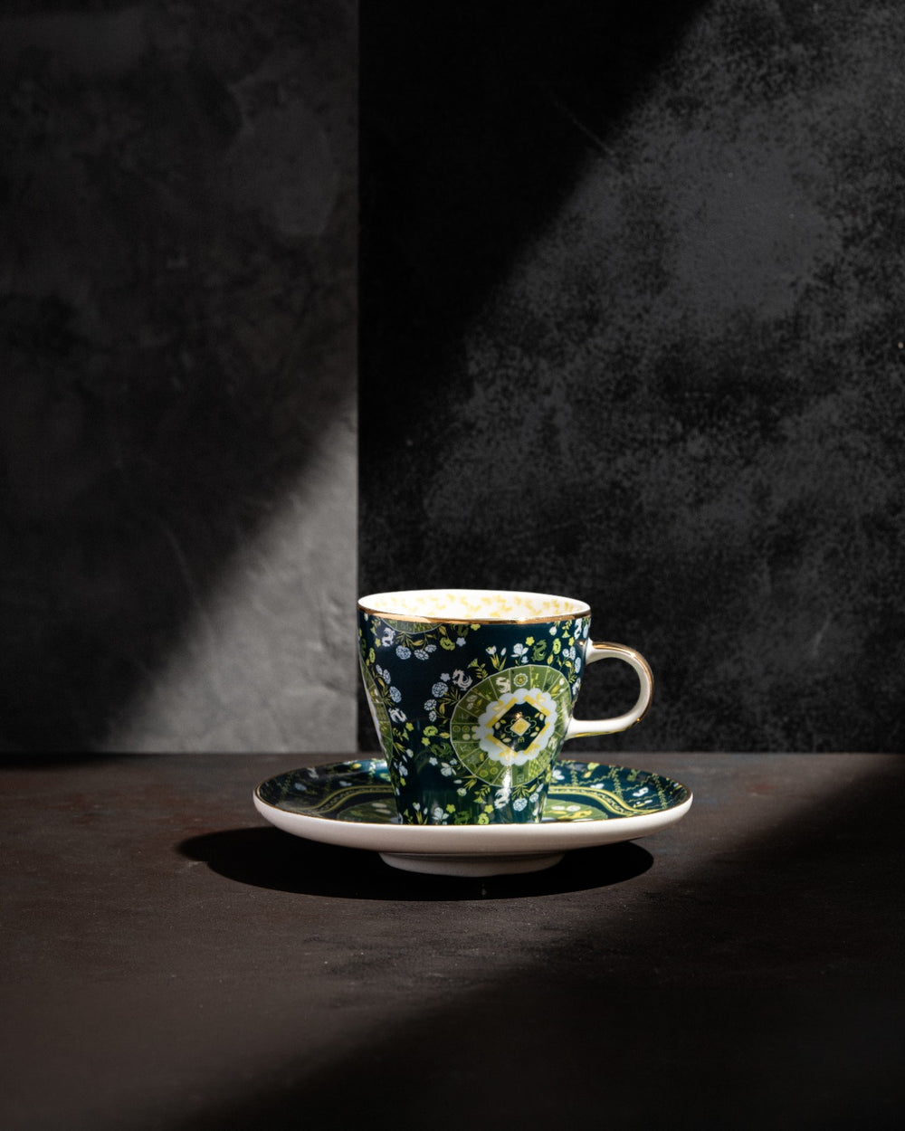 Navy ceramic teacup and saucer with green floral design, beige handle, dramatic studio lighting