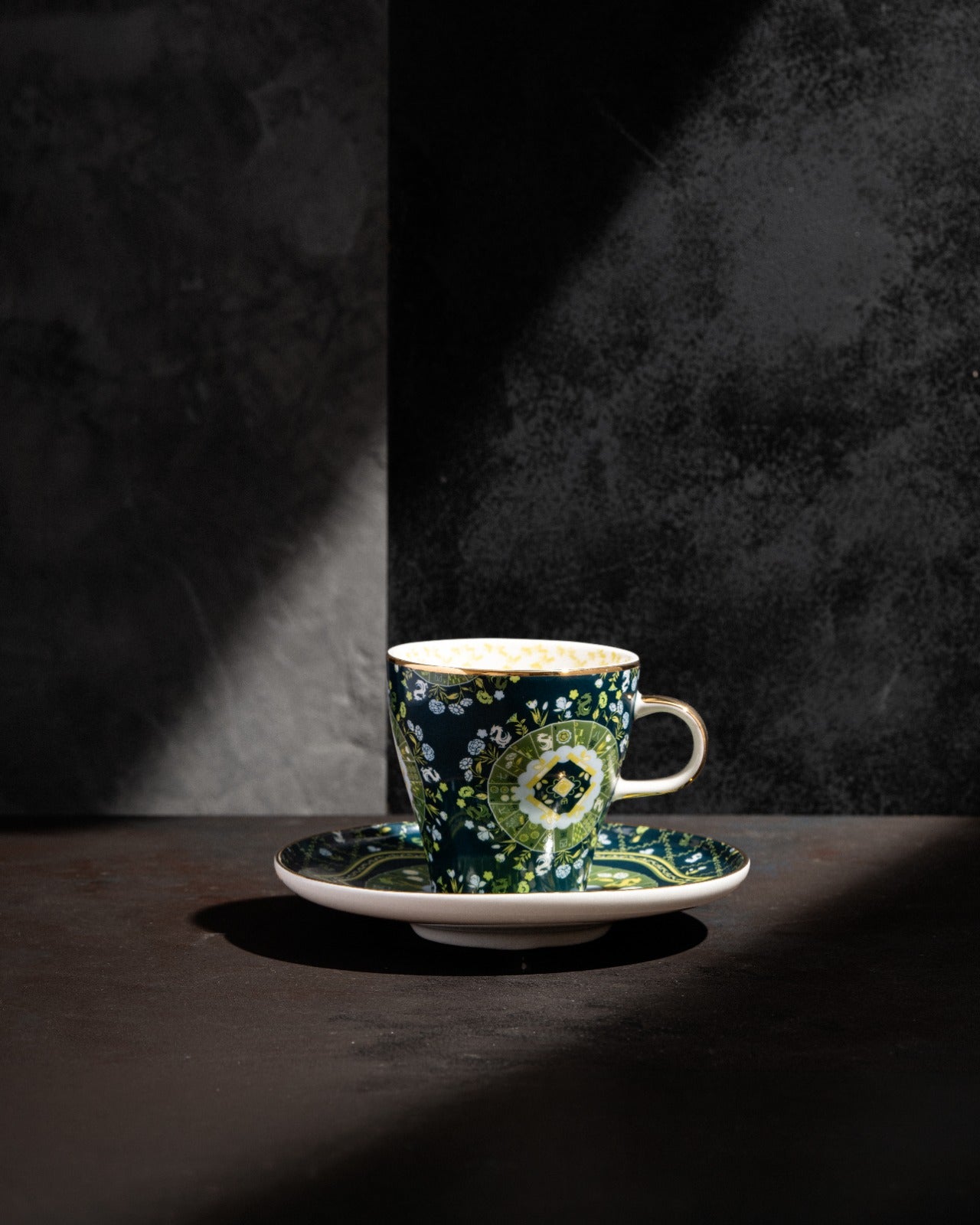 Navy ceramic teacup and saucer with green floral design, beige handle, dramatic studio lighting