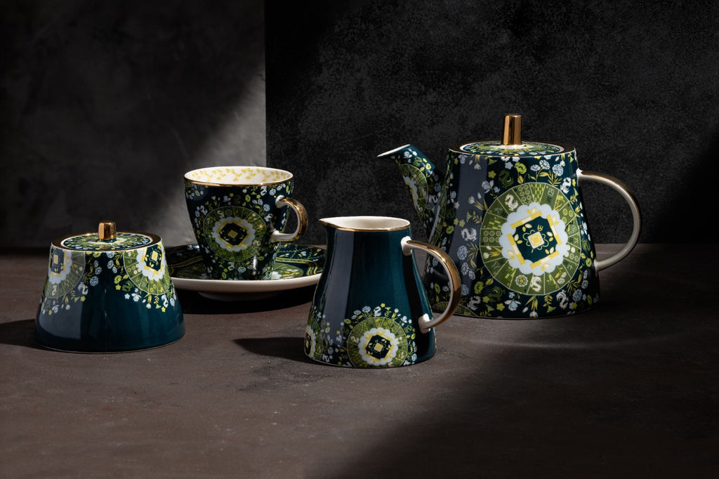 Teal ceramic tea set with green and white floral pattern, including teapot, cup and saucer, creamer, and lidded sugar bowl with wooden knobs